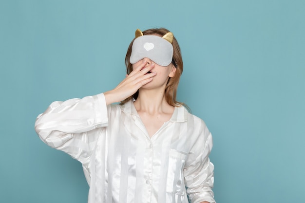 Photo gratuite jeune femme en pyjama et masque de sommeil bâillant sur bleu