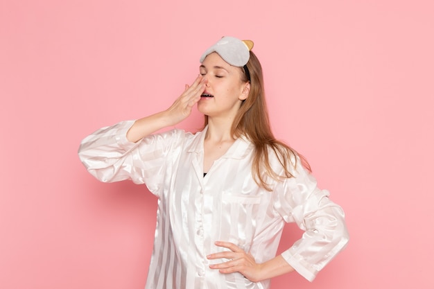 Jeune femme en pyjama et masque de sommeil bâillant mal sur rose
