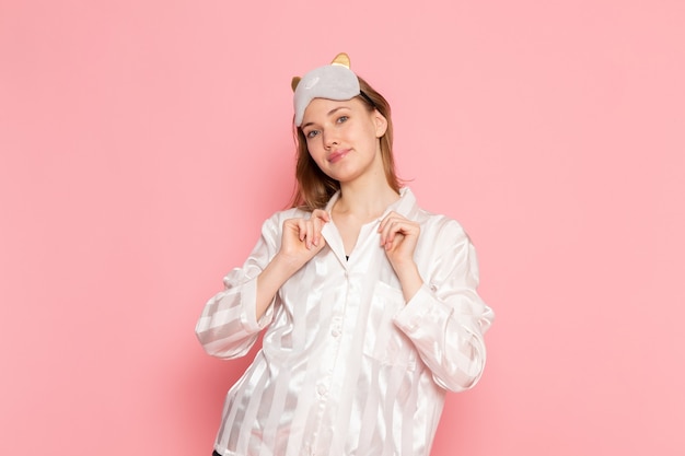 Photo gratuite jeune femme en pyjama et masque de sommeil debout et posant avec sourire sur rose