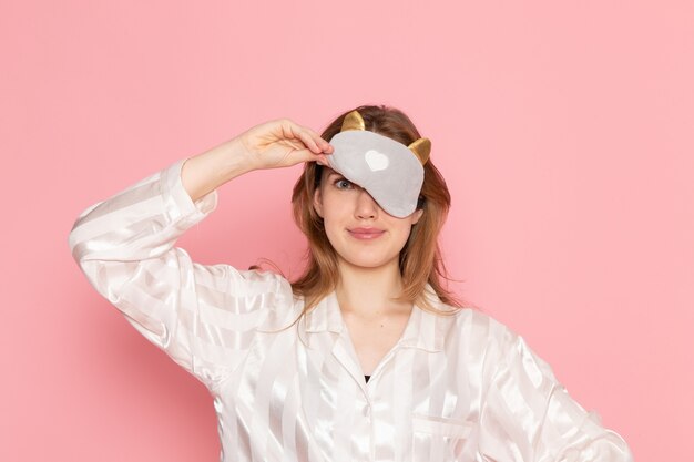 jeune femme en pyjama et masque de sommeil posant avec sourire sur rose