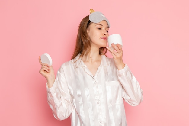 Jeune femme en pyjama et masque de sommeil sentant la crème sur rose