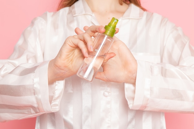 jeune femme en pyjama et masque de sommeil tenant un spray de maquillage sur rose