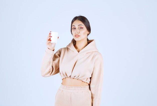 Jeune femme en pyjama rose tenant une tasse de boisson