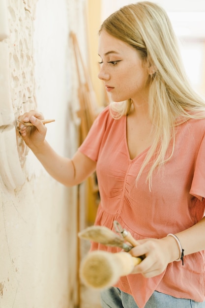 Jeune femme qualifiée sculptant sur le mur avec des outils