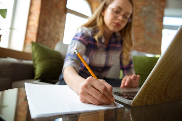 Jeune femme qui étudie à la maison pendant des cours en ligne ou des informations gratuites par elle-même en prenant des notes