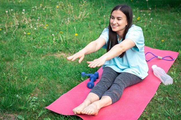 Photo gratuite une jeune femme qui s'étend en faisant des exercices de fitness dans un parc verdoyant