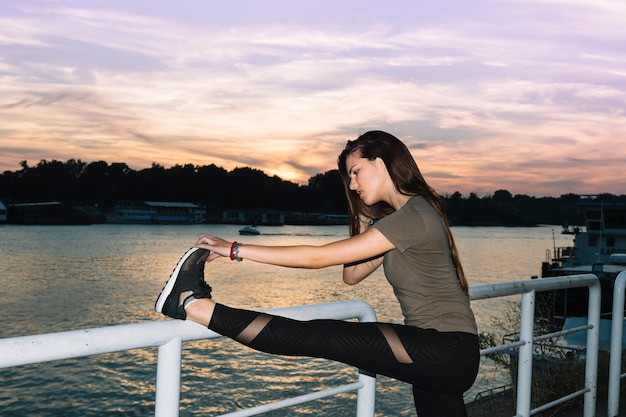 Jeune femme qui s&#39;étend de la jambe près de la rivière au coucher du soleil