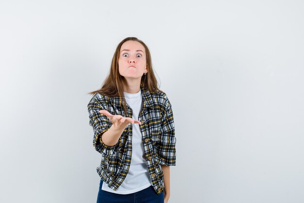 Jeune femme qui s'étend de la main dans le geste de questionnement en t-shirt, veste, jeans et à la colère, vue de face.