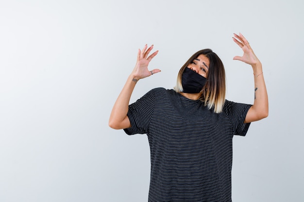 Jeune femme qui s'étend les mains comme tenant quelque chose en robe noire, masque noir et à la peur. vue de face.