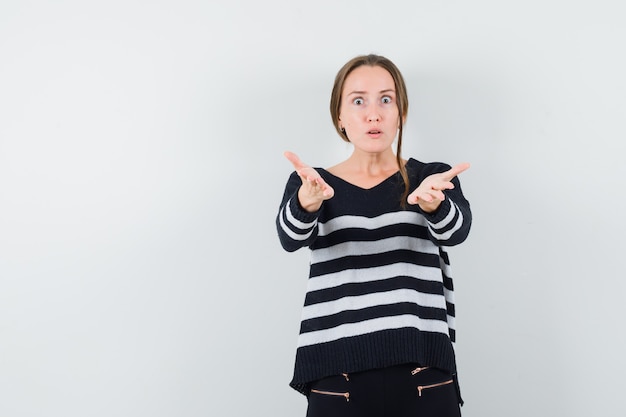 Jeune femme qui s'étend les mains vers l'avant en maille rayée et pantalon noir et à choqué