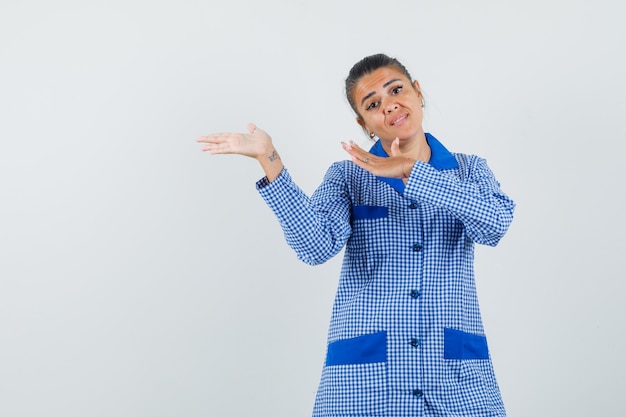 Jeune femme qui s'étend les mains vers la gauche en chemise de pyjama vichy bleu et à la jolie. vue de face.