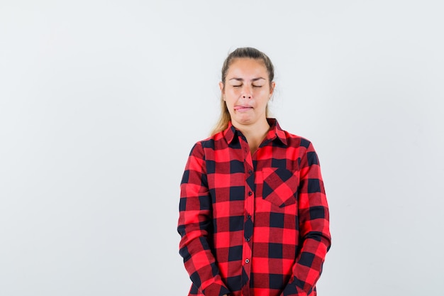 Jeune femme qui sort la langue en chemise à carreaux et à la rêveuse, vue de face.