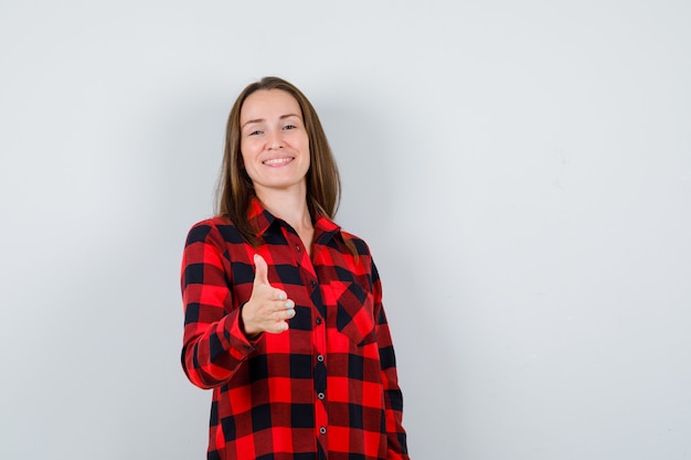 Jeune femme qui tend la main pour saluer quelqu'un en chemise à carreaux et à l'aimable. vue de face.