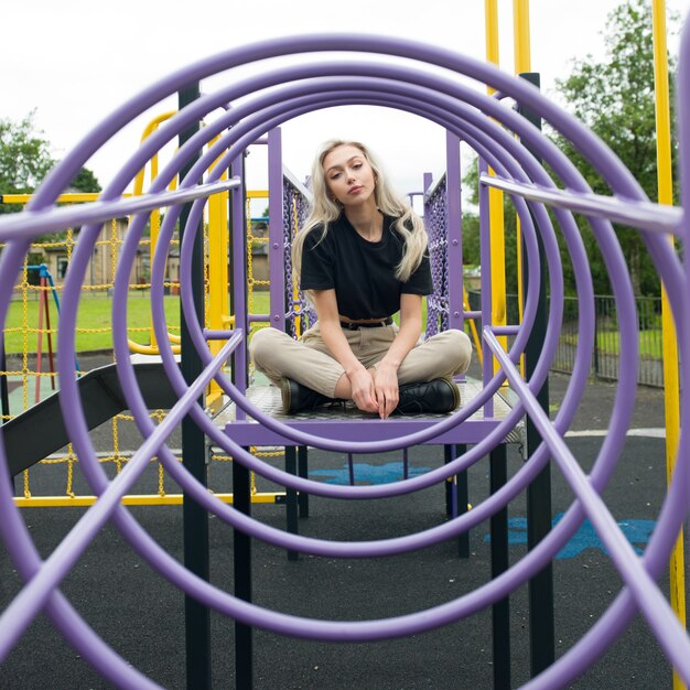 Jeune femme de race blanche assise dans une montée encerclée dans l'aire de jeux