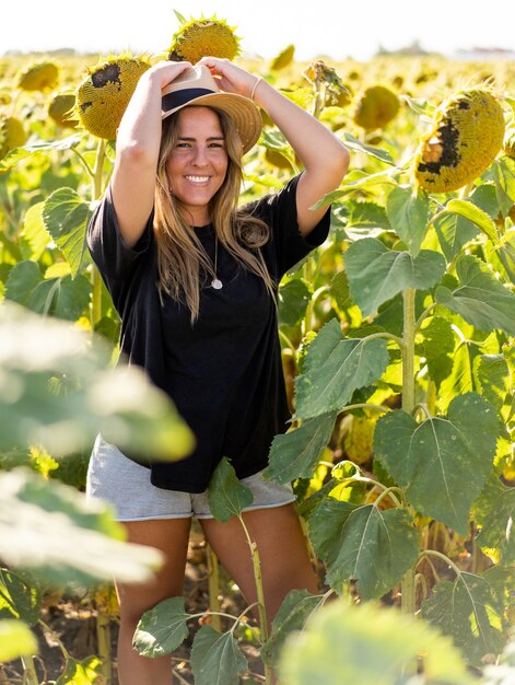 Jeune femme de race blanche avec un chapeau marchant dans un champ de tournesols sur une journée ensoleillée