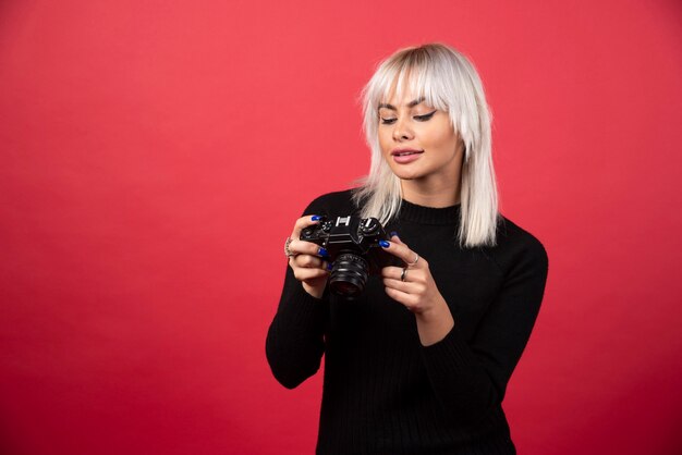 Jeune femme à la recherche d'un appareil photo sur fond rouge. Photo de haute qualité