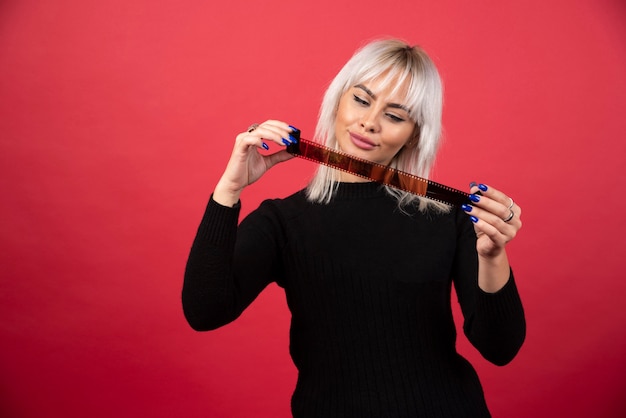 Jeune Femme à La Recherche D'une Cassette Photo Sur Fond Rouge. Photo De Haute Qualité