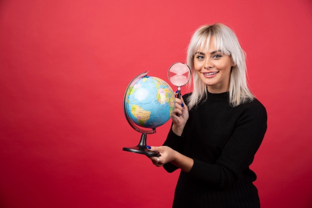 Jeune femme à la recherche sur un globe avec loupe sur fond rouge