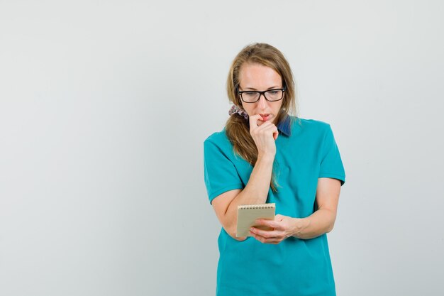 Jeune femme à la recherche de notes sur cahier en t-shirt et à la pensif.