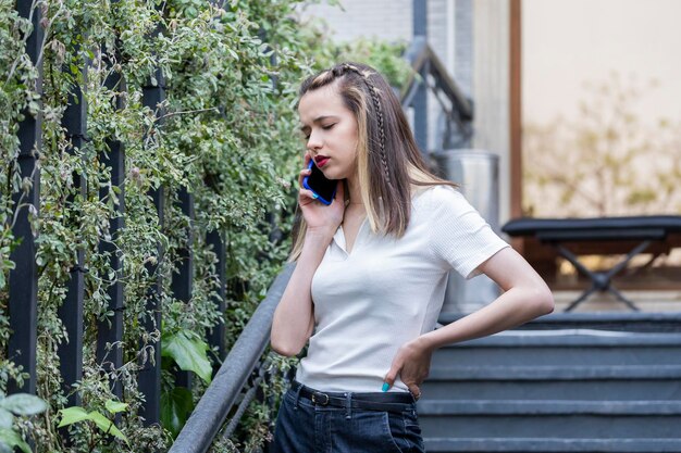 Jeune femme réfléchie debout dans les escaliers et parlant au téléphone