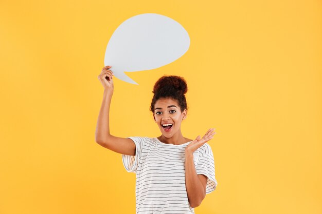 Jeune femme réfléchie heureuse africaine et tenant une bulle de dialogue vide isolé sur jaune