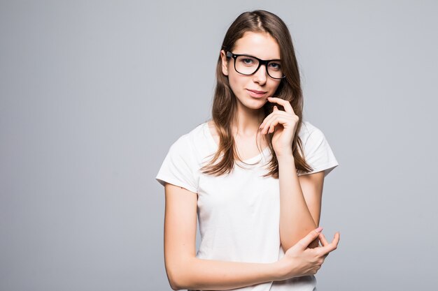 Jeune femme de réflexion sérieuse dans des verres en t-shirt blanc et blue-jeans rester en face de fond de studio blanc