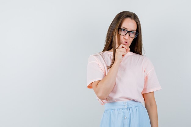 Jeune femme regardant ailleurs en t-shirt, jupe et à la pensive. vue de face.