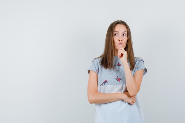 Jeune femme regardant ailleurs en t-shirt et regardant pensif, vue de face.