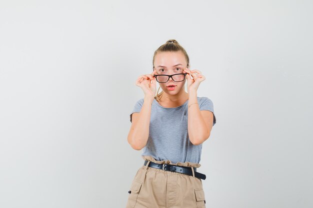 Jeune femme regardant attentivement sur des lunettes en t-shirt, pantalon, vue de face.