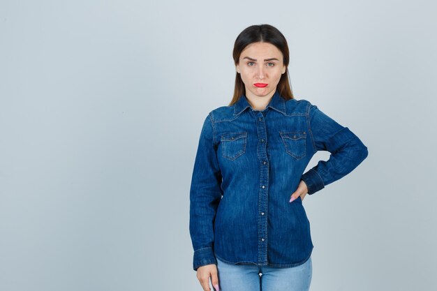 Jeune femme regardant avant tout en gardant la main sur la hanche en chemise en jean et jeans et à l'offensé