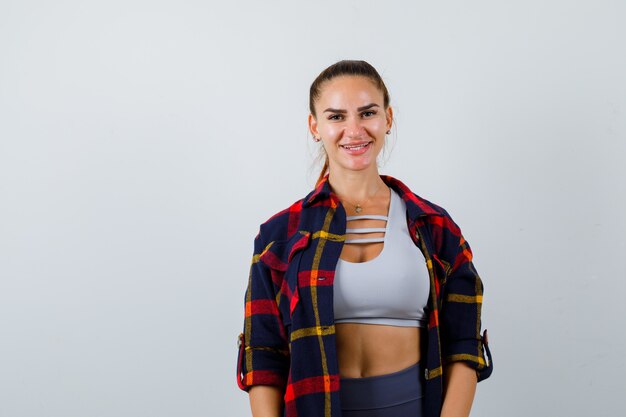 Jeune femme regardant la caméra en haut court, chemise à carreaux, pantalon et l'air heureux, vue de face.