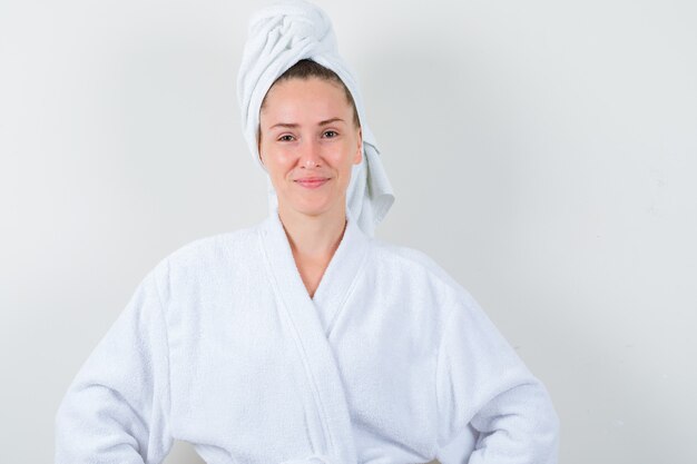 Jeune femme regardant la caméra en peignoir blanc, serviette et à la joyeuse, vue de face.