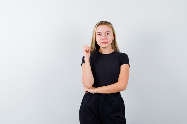 Jeune femme regardant la caméra tout en posant en t-shirt, pantalon et à la joyeuse vue de face.