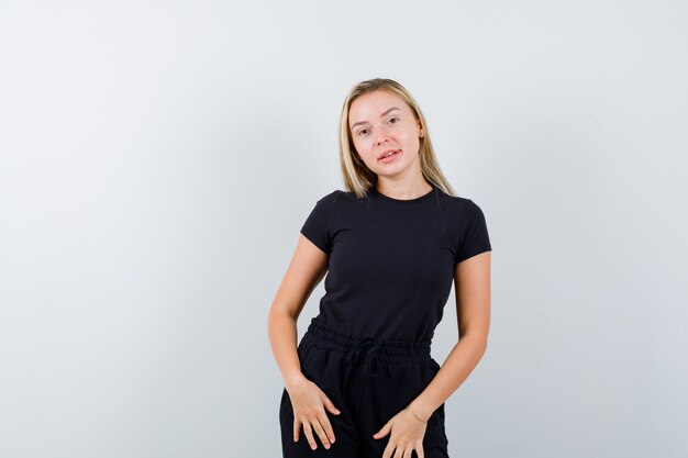 Jeune femme regardant la caméra tout en posant en t-shirt, pantalon et à la recherche de mignon. vue de face.