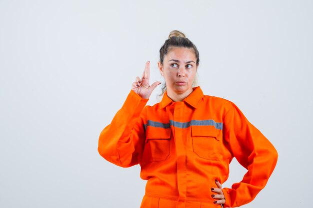 Jeune femme regardant de côté tout en croisant ses doigts en uniforme de travailleur et regardant pensif, vue de face.