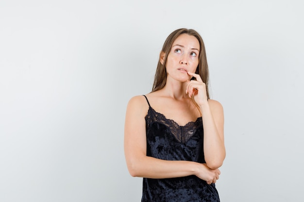 Jeune femme regardant avec le doigt près de la bouche en maillot noir et à la réflexion