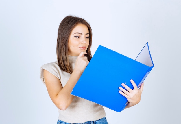 Jeune femme regardant un dossier bleu sur fond blanc.