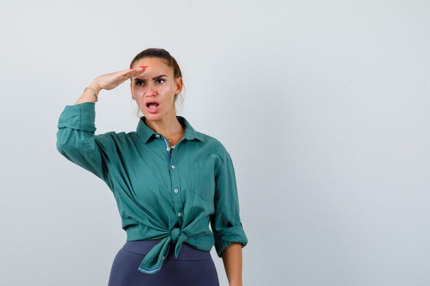 Jeune femme regardant loin avec la main sur la tête en chemise verte et l'air choquée. vue de face.