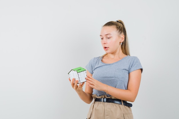 Jeune femme regardant le modèle de la maison en t-shirt et pantalon et à la surprise