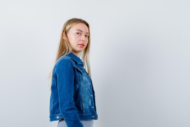 Jeune femme regardant par-dessus l'épaule en t-shirt, veste en jean, jupe et magnifique