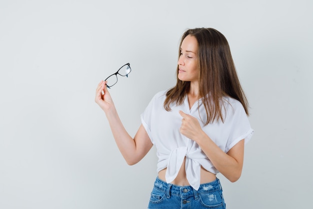 Jeune femme regardant ses lunettes en vue de face de chemisier blanc.