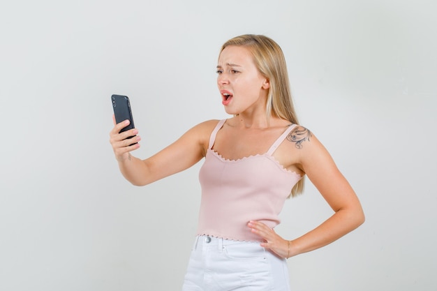 Jeune femme regardant smartphone en maillot, mini jupe et à la recherche de désolé.