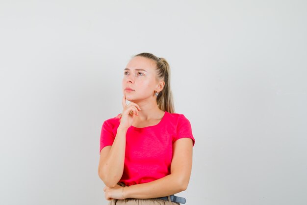 Jeune femme regardant en t-shirt, pantalon et à la pensif. vue de face.