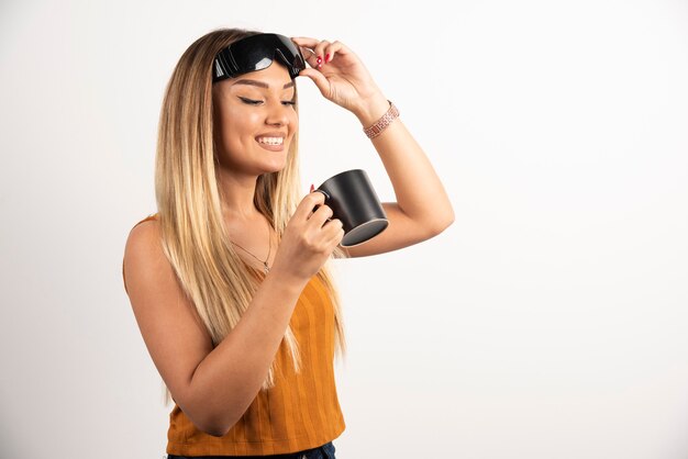 Jeune femme regardant une tasse noire et portant des lunettes.