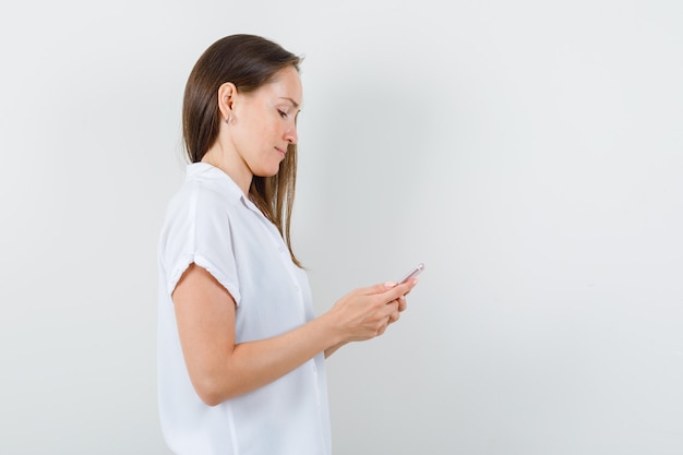 Jeune femme regardant le téléphone en chemisier blanc et à la recherche concentrée