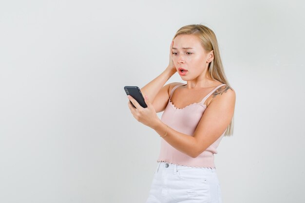 Jeune femme regardant un téléphone mobile en maillot, mini jupe et à la recherche de regret.