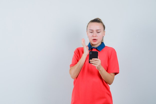 Jeune femme regardant un téléphone mobile en t-shirt et à la confusion