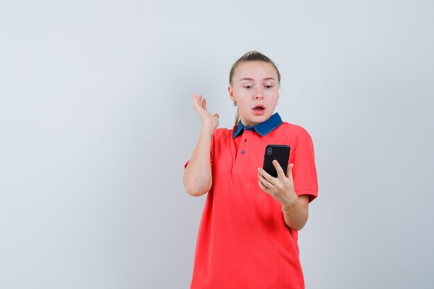 Jeune femme regardant un téléphone mobile en t-shirt et à la surprise