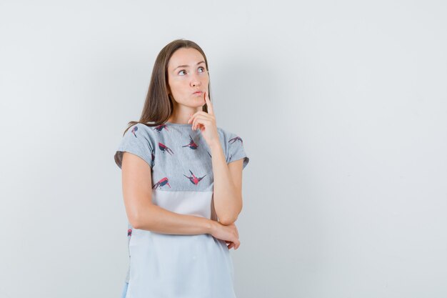 Jeune femme regardant tout en pensant en t-shirt et à la vue indécise, de face.