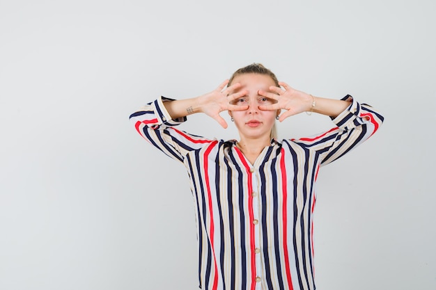 Jeune femme regardant à travers les doigts en chemise rayée et à la jolie